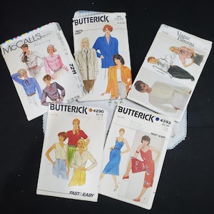 May include: A collection of six sewing patterns for clothing. The patterns are from McCall's, Vogue, and Butterick. The patterns are for tops, dresses, and pants. The patterns are in various colors, including white, blue, red, and green.