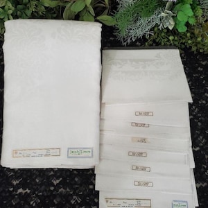 May include: A set of white Irish linen napkins and a matching tablecloth featuring a subtle damask floral pattern. Each piece includes a rectangular label with the text Irish Linen, Made in Ireland, and details regarding the fabric composition.