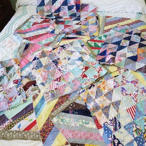 Può includere: Una collezione di trapunte patchwork colorate con vari motivi geometrici. Le trapunte presentano un mix di pezzi di tessuto floreale, a righe e tinta unita in tonalità di blu, rosa, giallo e verde. Le trapunte sono disposte su un copriletto bianco.