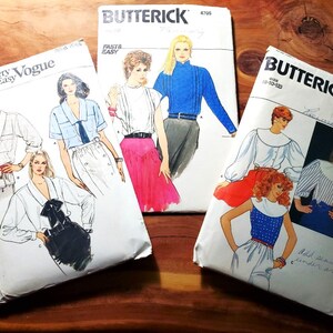 May include: Three vintage sewing patterns for blouses. The patterns are from the brand Butterick and feature different styles of blouses with collars and long sleeves. The patterns are in various colors, including white, blue, and red.