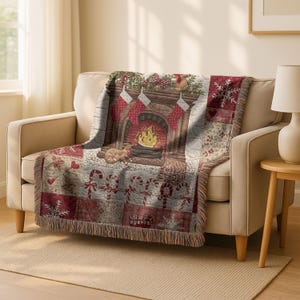 May include: A woven throw blanket featuring a Christmas fireplace scene with stockings, a burning fire, and candy canes. The blanket is primarily red, white, and brown, with a fringed edge. The blanket is draped over a beige loveseat.