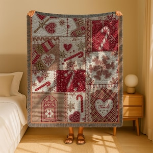 May include: A Christmas-themed throw blanket with a patchwork design. The blanket features squares with red and white patterns, including hearts, snowflakes, and candy canes. The blanket has a fringed edge and is held up by a person.