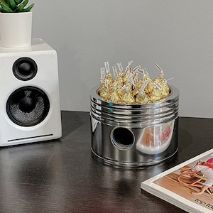 Puede incluir: Un recipiente de metal plateado con forma de pistón de motor de coche, lleno de besos de chocolate envueltos en papel de oro.