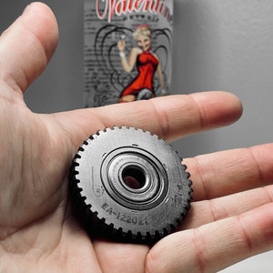 May include: A metal gear with a toothed outer edge and a central bearing. The gear has the markings "EA-122021" and "S.A.B.R." The background features a Valentine's Day themed image.