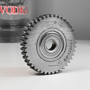 Könnte beinhalten: Ein silbernes Zahnrad mit einem großen, zentralen Lager und einer gezahnten Kante. Das Zahnrad ist mit dem Text "EA-12202" gekennzeichnet.