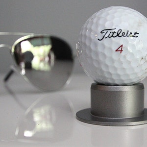 May include: A white golf ball with the text "Titleist 4" printed on it. The golf ball is sitting on a silver stand.