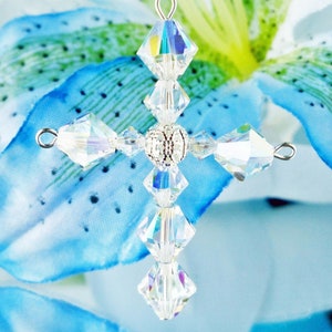May include: A crystal cross pendant with a silver bead in the center. The cross is made of clear faceted crystals and is hanging from a silver chain.