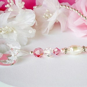 May include: A pink and clear crystal car charm with a pearl and silver beads. The charm is hanging from a silver chain.