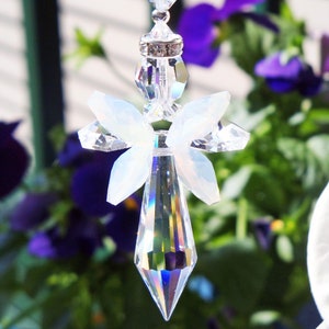 May include: A crystal suncatcher with a clear teardrop-shaped prism and a white angel wing design. The suncatcher is hanging from a chain with clear crystal beads.
