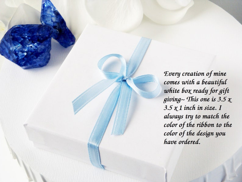 May include: A white gift box with a light blue ribbon tied in a bow. The box is 3.5 x 3.5 x 1 inches in size. The text on the box reads: "Every creation of mine comes with a beautiful white box ready for gift giving~ This one is 3.5 x 3.5 x 1 inch in size. I always try to match the color of the ribbon to the color of the design you have ordered."