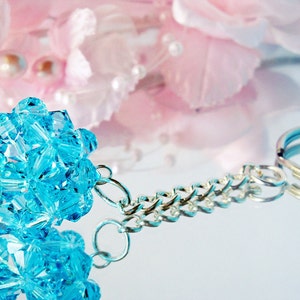 May include: A turquoise blue crystal charm attached to a silver chain with a silver key ring.