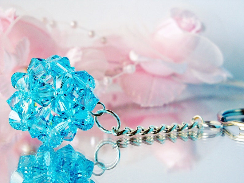 May include: A light blue crystal keychain with a silver chain. The crystal is shaped like a ball and is made up of many small, faceted pieces.