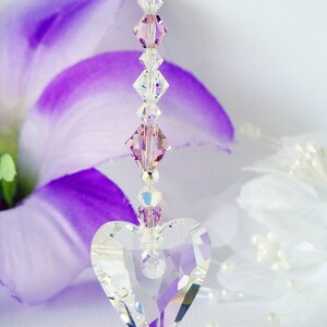 Puede incluir: Un atrapasol en forma de coraz&oacute;n de cristal con una cadena de cuentas de cristal morado y transparente. El atrapasol est&aacute; colgado de un cristal morado.