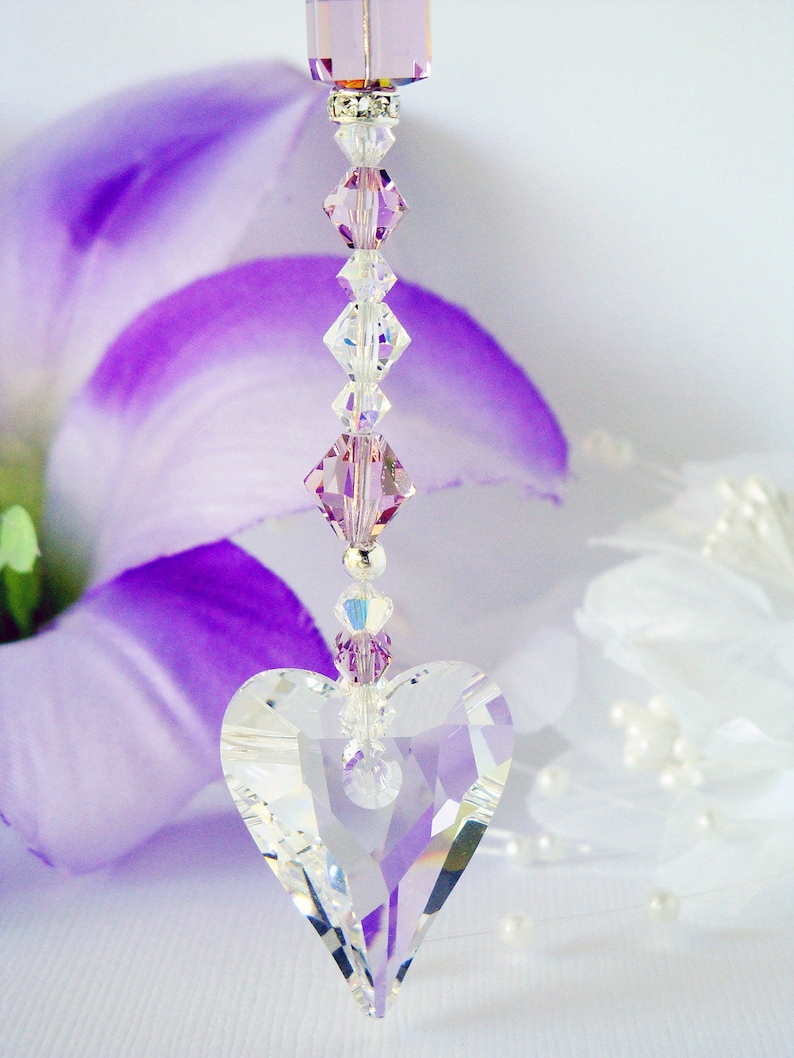 Puede incluir: Un atrapasol en forma de coraz&oacute;n de cristal con una cadena de cuentas de cristal morado y transparente. El atrapasol est&aacute; colgado de un cristal morado.
