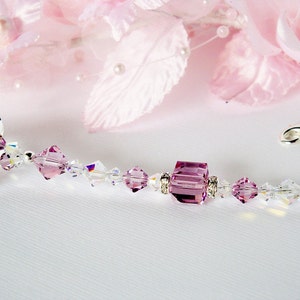 Puede incluir: Un delicado collar de cristal con una gran cuenta de cristal cuadrada de color amatista en el centro. El collar est&aacute; hecho con peque&ntilde;as cuentas de cristal transparentes y detalles plateados.