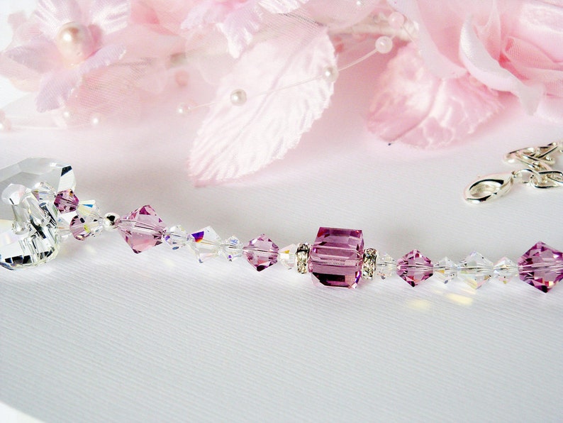 Puede incluir: Un delicado collar de cristal con una gran cuenta de cristal cuadrada de color amatista en el centro. El collar est&aacute; hecho con peque&ntilde;as cuentas de cristal transparentes y detalles plateados.