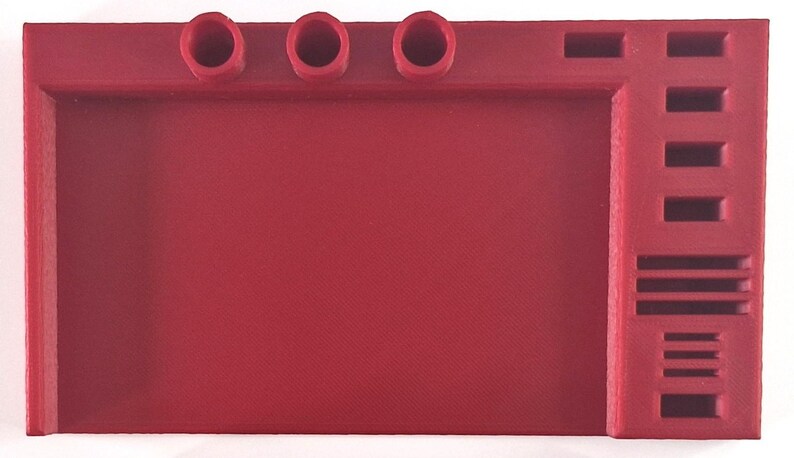 May include: A solid red desk organizer with three circular pen holders, a large open space, and a side section with multiple rectangular slots. The organizer is made of a matte material.