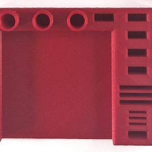 May include: A solid red, 3D-printed desk organizer. The organizer features three circular holes, a rectangular slot, and several rectangular and horizontal slots. The design is angular and modern, suitable for office or home use.