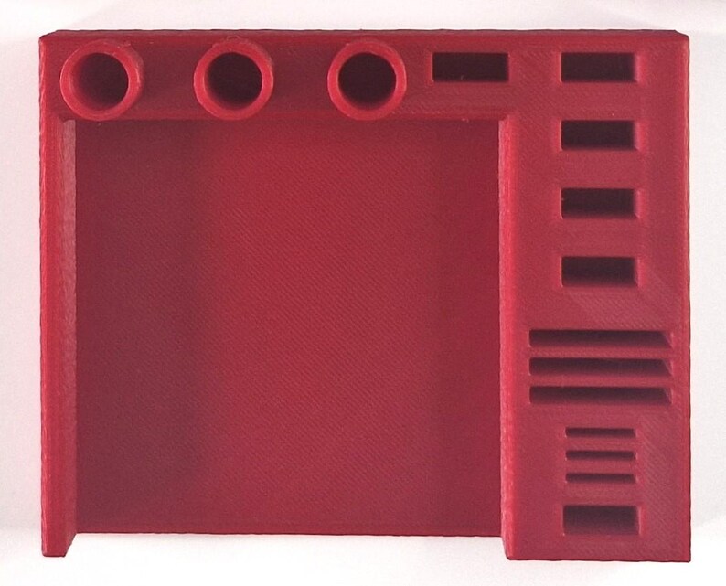 May include: A solid red, 3D-printed desk organizer. The organizer features three circular holes, a rectangular slot, and several rectangular and horizontal slots. The design is angular and modern, suitable for office or home use.