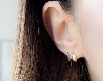 May include: A woman wearing a gray blazer with a herringbone pattern. She is wearing two small hoop earrings in her left ear. The earrings are gold and silver.