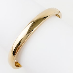 Puede incluir: Una pulsera rígida articulada de tono dorado pulido con una superficie lisa y redondeada y un mecanismo de cierre seguro. La pulsera presenta un diseño de banda metálica sólida y continua con un acabado brillante y reflectante.