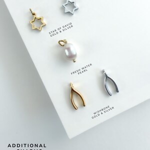 May include: A collection of jewellery charms including gold and silver Star of David charms, a white freshwater pearl charm, and gold and silver wishbone charms. The text reads ADDITIONAL CHARMS OPTIONS, STAR OF DAVID GOLD & SILVER, FRESH WATER PEARL, and WISHBONE GOLD & SILVER.