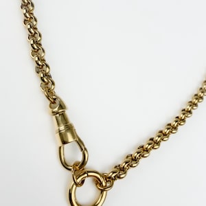 May include: A gold-toned chain necklace featuring a series of rounded, interlocking links. The necklace includes a prominent swivel lobster clasp mechanism attached to a circular ring, providing a secure closure for the polished metal chain.