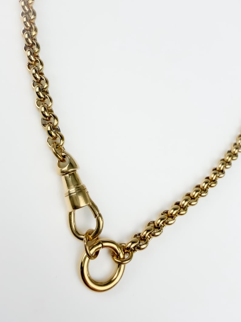 May include: A gold-toned chain necklace featuring a series of rounded, interlocking links. The necklace includes a prominent swivel lobster clasp mechanism attached to a circular ring, providing a secure closure for the polished metal chain.