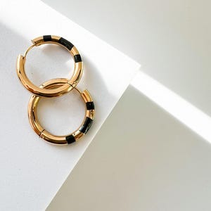 May include: A pair of gold hoop earrings with black accents. The earrings are thick and have a rounded shape.