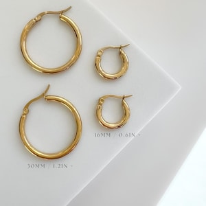 May include: Four gold-colored hoop earrings of varying sizes are displayed on a white surface. The larger hoops are 30mm (1.2 inches) in diameter, while the smaller ones are 16mm (0.6 inches). The earrings have a classic, polished design.