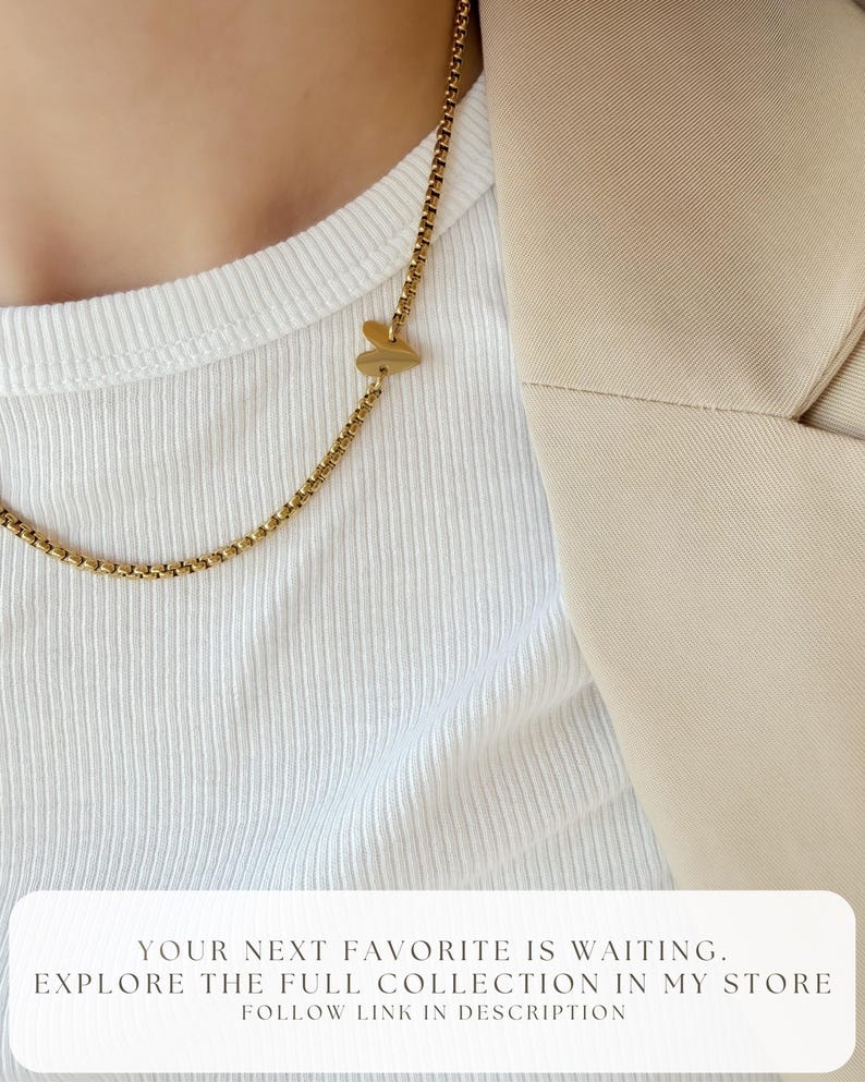 May include: A gold-toned box chain necklace featuring a small, smooth heart-shaped charm. The text at the bottom reads: YOUR NEXT FAVORITE IS WAITING. EXPLORE THE FULL COLLECTION IN MY STORE. FOLLOW LINK IN DESCRIPTION.