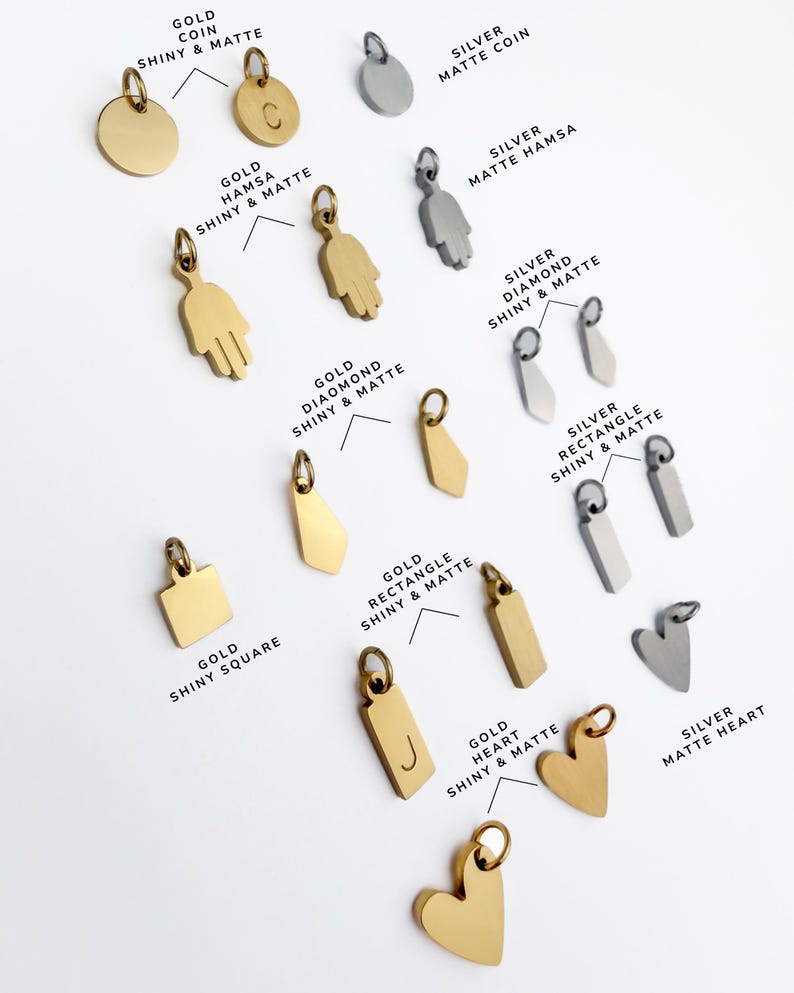 Puede incluir: Una colecci&oacute;n de dijes de metal en tonos oro y plata, con diversas formas que incluyen monedas, manos de hamsa, diamantes, rect&aacute;ngulos, cuadrados y corazones. Algunos dijes son brillantes, otros mate, con algunas piezas grabadas con letras.