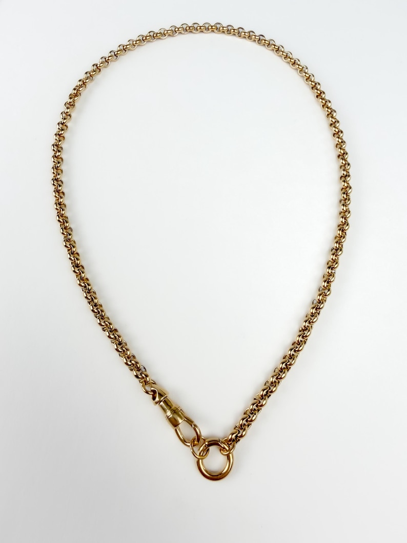 May include: A gold-toned chain necklace featuring a series of interlocking circular links. The necklace includes a swivel lobster clasp mechanism attached to a circular ring, allowing for a secure closure and a classic, uniform link design.