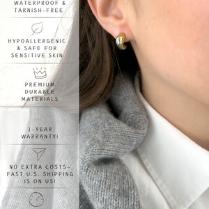 May include: A close-up of a gold and silver hoop earring on an ear. The earring is a small, curved design. Text on the left side of the image reads: Waterproof & Tarnish-Free, Hypoallergenic & Safe for Sensitive Skin, Premium Durable Materials.