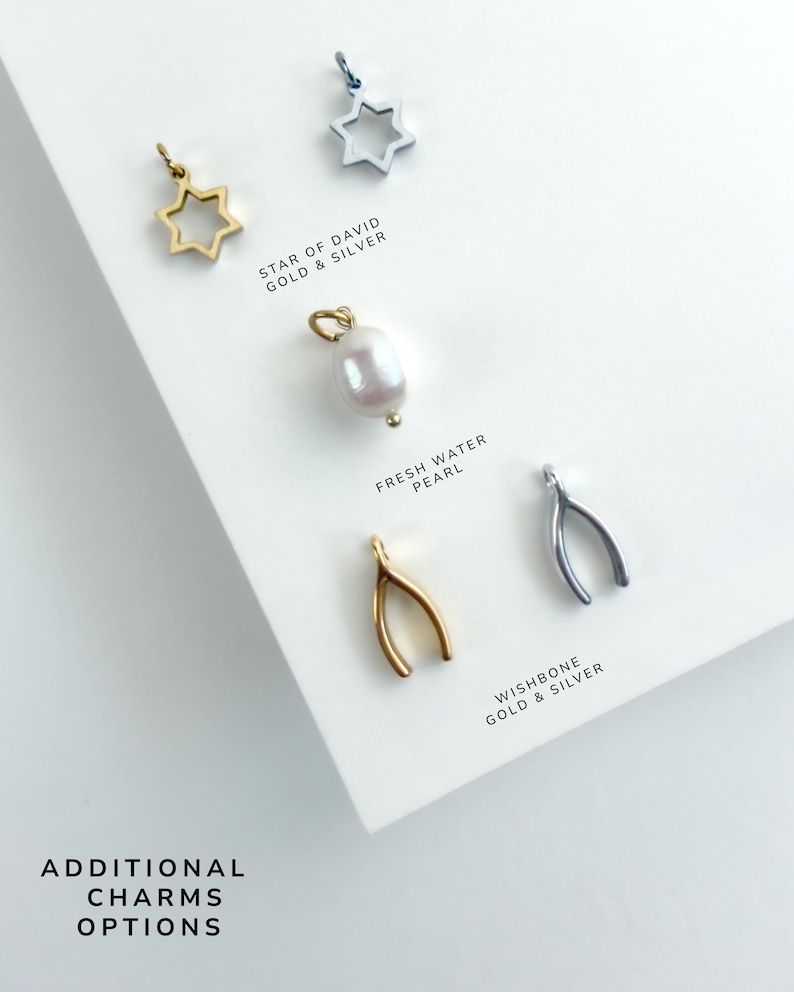 May include: A collection of jewelry charms including gold and silver Star of David charms, a white freshwater pearl charm, and gold and silver wishbone charms. Text labels read STAR OF DAVID GOLD & SILVER, FRESH WATER PEARL, WISHBONE GOLD & SILVER, and ADDITIONAL CHARMS OPTIONS.