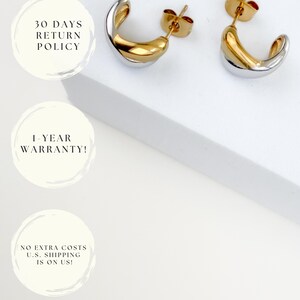 May include: A pair of two-tone gold and silver hoop earrings. The earrings have a curved design with a gold interior and a silver exterior. The earrings are displayed on a white surface.