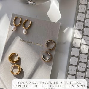 Flat lay of multiple NONO SF hoop earrings on neutral surface near a keyboard. Everyday gold earring styles built for mixing and matching.