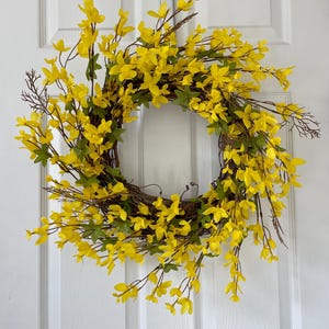 May include: A yellow floral wreath with green leaves. The wreath is made of artificial flowers and is perfect for spring decor.