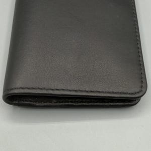 May include: A dark gray leather wallet with a stitched border. The wallet is closed and appears to be empty. The leather has a subtle texture and a matte finish.