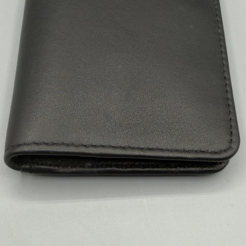 May include: A dark gray leather wallet with a stitched border. The wallet is closed and appears to be empty. The leather has a subtle texture and a matte finish.