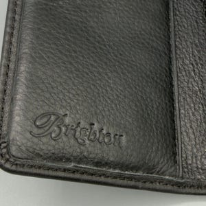 May include: Close-up of a black leather wallet with the embossed word "Brighton" in a cursive font. The leather has a textured appearance, and the wallet appears to be closed.