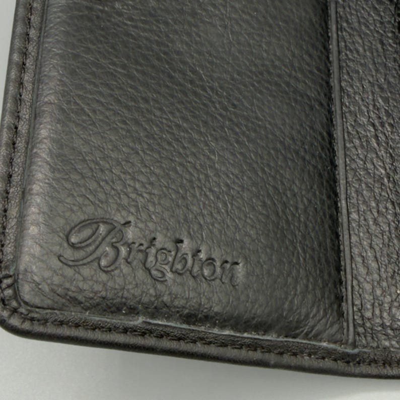 May include: Close-up of a black leather wallet with the embossed word "Brighton" in a cursive font. The leather has a textured appearance, and the wallet appears to be closed.