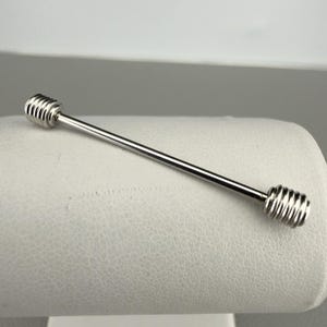 May include: A silver-toned metal collar bar featuring a straight, slender rod with a polished finish and two cylindrical, ribbed screw-on end caps. The accessory has a clean, metallic appearance with a smooth central shaft and textured ends.