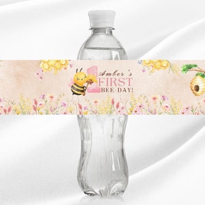 May include: Water bottle label with a bee and honeycomb design. The label says "Amber's First Bee-Day!"