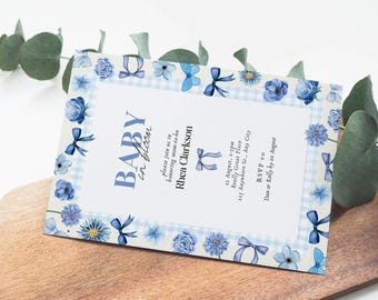 Peut inclure: Une invitation de fête prénatale bleu et blanc avec un motif vichy et des fleurs bleues. Le texte indique "Baby in Bloom" et comprend la date, l'heure et le lieu de l'événement. Les informations de RSVP sont également incluses.