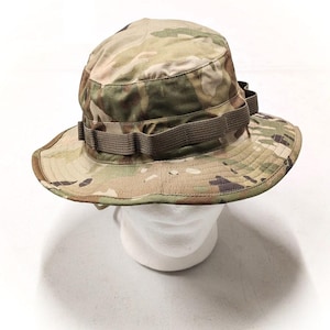 May include: A camouflage-patterned boonie hat with a brown adjustable strap. The hat is made of a lightweight fabric and has a wide brim.