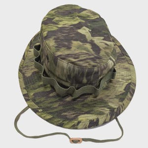 May include: A green and brown camouflage boonie hat with a wide brim and a chin strap. The hat features a circular crown and a band of fabric loops around the sides. The hat is made of a durable, lightweight material.