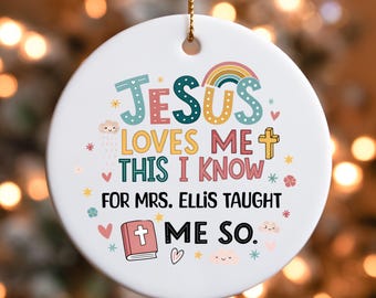 May include: A white, round Christmas ornament with the text "JESUS LOVES ME THIS I KNOW FOR MRS. ELLIS TAUGHT ME SO." in colorful letters. The ornament features a rainbow, cross, hearts, stars, and a book illustration.