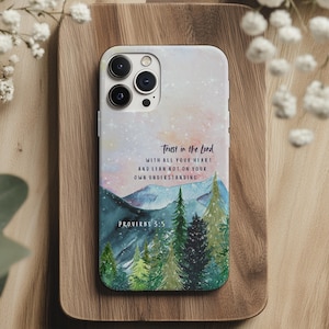 May include: A smartphone case featuring a watercolor-style landscape of mountains and pine trees under a starry sky. The text reads: Trust in the Lord with all your heart and lean not on your own understanding. Proverbs 3:5 is printed below.