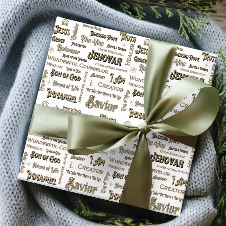 May include: A wrapped gift with white paper featuring religious words in a repeating pattern, including "Jesus" and "Savior." The gift is tied with a sage green satin ribbon and bow, creating a festive presentation.